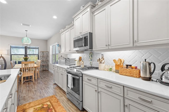 kitchen with decorative light fixtures, backsplash, appliances with stainless steel finishes, and light hardwood / wood-style flooring