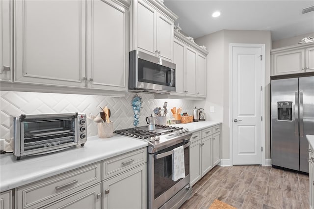 kitchen with appliances with stainless steel finishes, backsplash, and light hardwood / wood-style floors