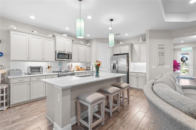 kitchen featuring stainless steel appliances, sink, pendant lighting, a center island with sink, and light hardwood / wood-style flooring