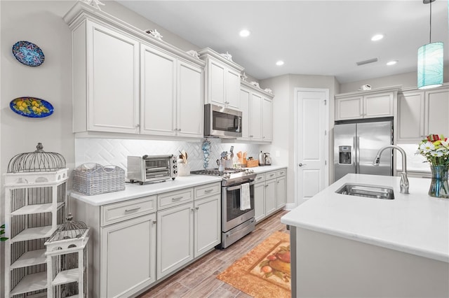 kitchen with sink, stainless steel appliances, light hardwood / wood-style flooring, backsplash, and decorative light fixtures