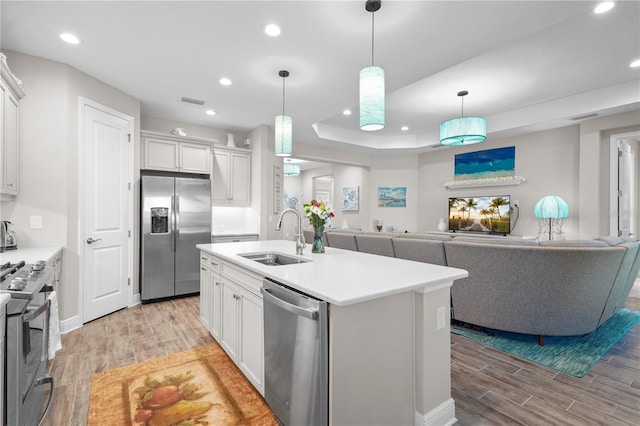 kitchen featuring appliances with stainless steel finishes, light wood-type flooring, a kitchen island with sink, sink, and white cabinets