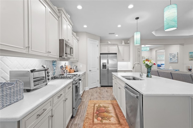 kitchen featuring appliances with stainless steel finishes, sink, decorative light fixtures, light hardwood / wood-style floors, and white cabinetry