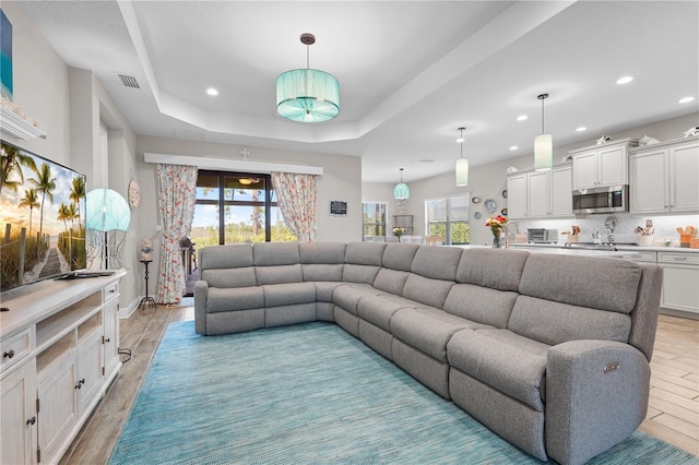 living room featuring a tray ceiling, plenty of natural light, and light hardwood / wood-style flooring