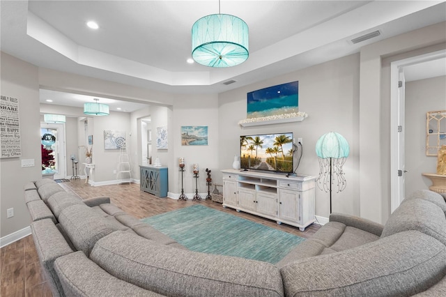 living room with wood-type flooring and a tray ceiling