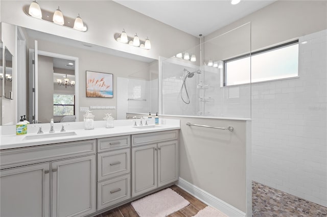 bathroom featuring wood-type flooring, vanity, an inviting chandelier, and a tile shower