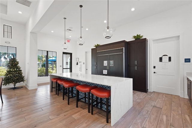 kitchen featuring pendant lighting, a breakfast bar, paneled built in fridge, a spacious island, and a towering ceiling