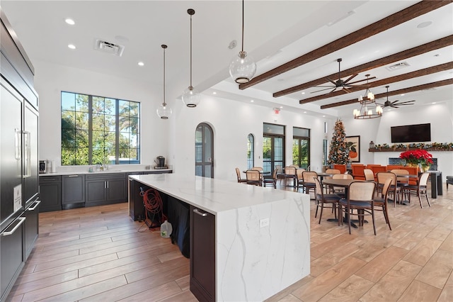 kitchen with light stone counters, a spacious island, pendant lighting, light hardwood / wood-style flooring, and beamed ceiling