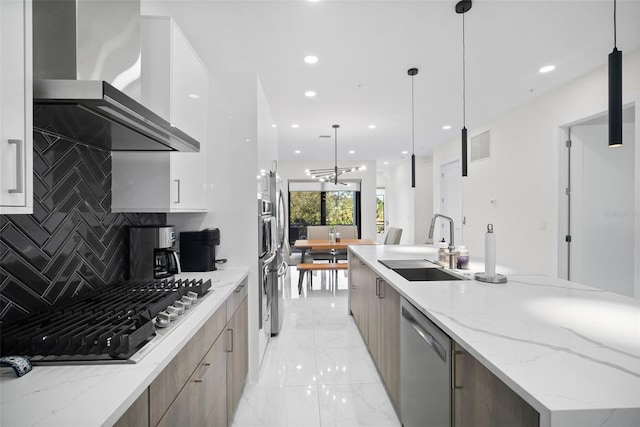 kitchen featuring decorative backsplash, appliances with stainless steel finishes, light stone counters, wall chimney range hood, and pendant lighting