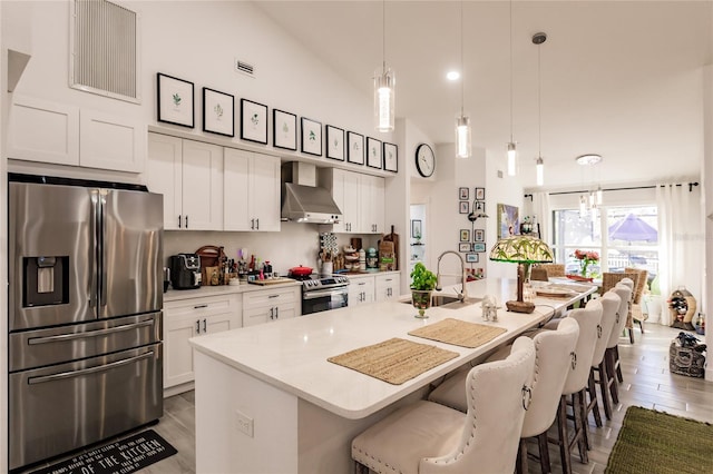 kitchen featuring sink, stainless steel appliances, a kitchen island with sink, and wall chimney range hood