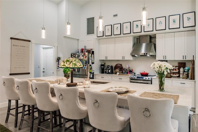 kitchen with wall chimney exhaust hood, a kitchen bar, a towering ceiling, and appliances with stainless steel finishes