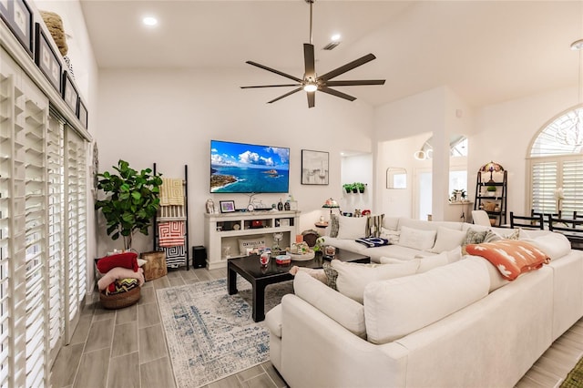 living room featuring ceiling fan, a high ceiling, and light wood-type flooring