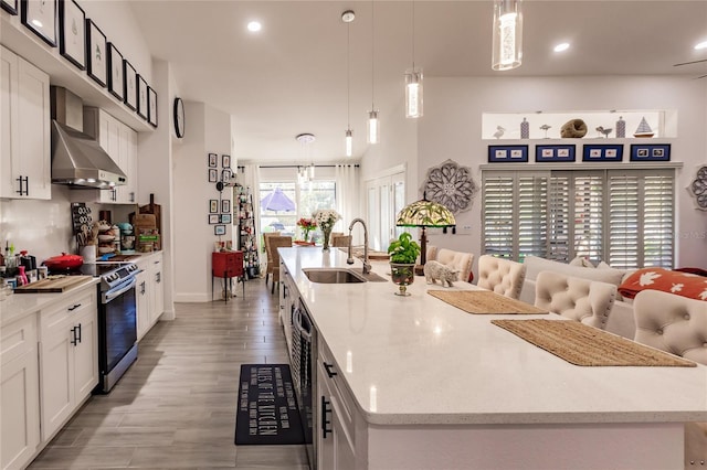 kitchen with a kitchen island with sink, sink, wall chimney range hood, pendant lighting, and stainless steel range oven