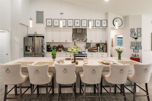 kitchen with a kitchen breakfast bar, stainless steel fridge, hanging light fixtures, and wall chimney range hood