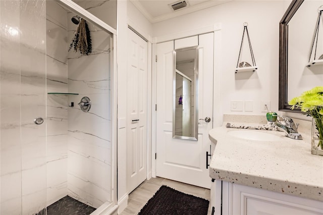 bathroom featuring vanity, a tile shower, ornamental molding, and wood-type flooring