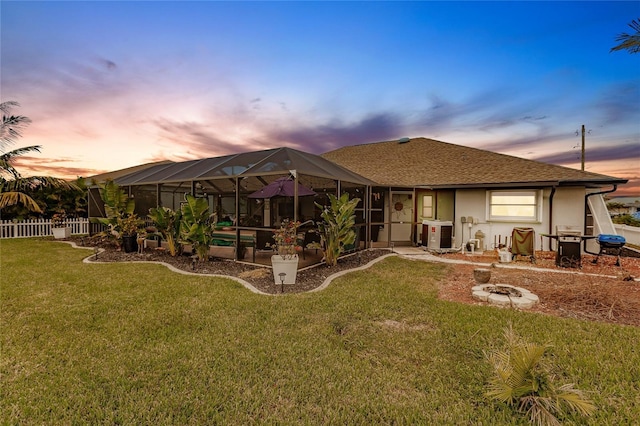 back house at dusk featuring a yard, cooling unit, and a lanai