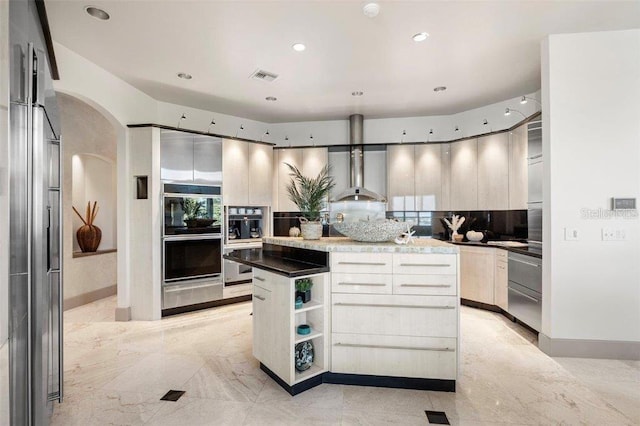 kitchen featuring wall chimney exhaust hood, stainless steel double oven, black double oven, decorative backsplash, and a kitchen island