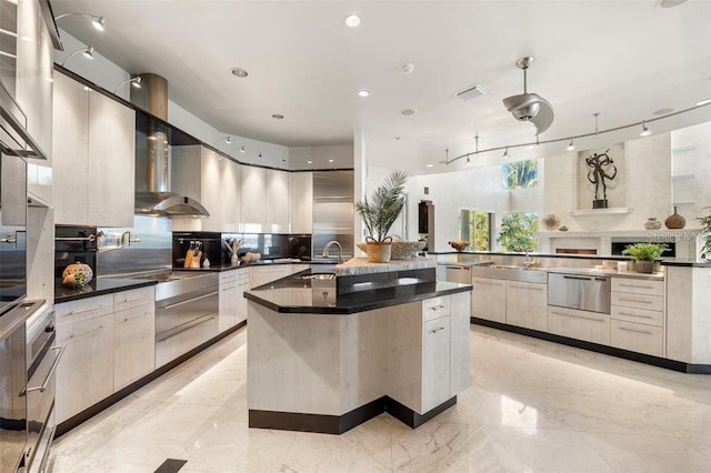 kitchen featuring stainless steel fridge, sink, a spacious island, and wall chimney range hood