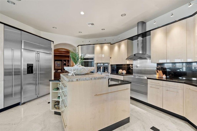 kitchen featuring built in fridge, wall chimney exhaust hood, tasteful backsplash, black oven, and a kitchen island