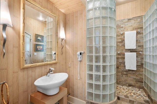 bathroom with tiled shower, sink, wooden walls, and wood ceiling