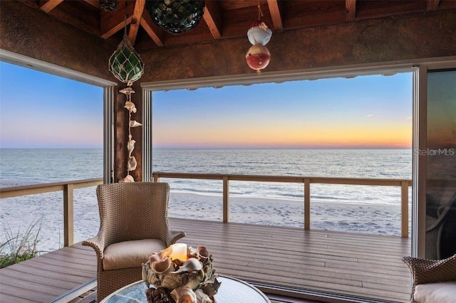 balcony at dusk featuring a view of the beach and a water view