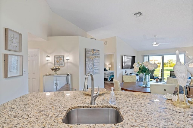 kitchen featuring lofted ceiling, light stone countertops, visible vents, and a sink