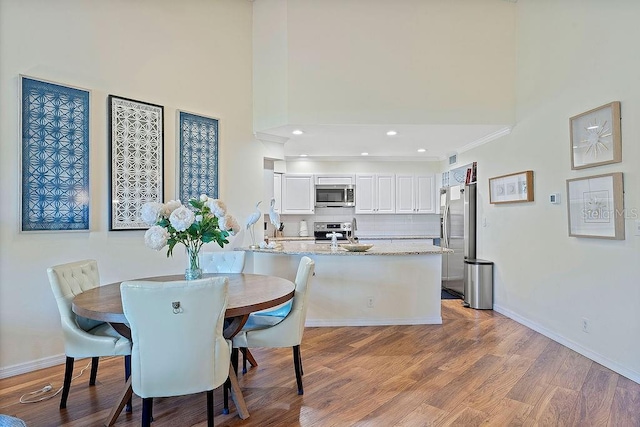 dining space with a towering ceiling, light wood finished floors, baseboards, and recessed lighting