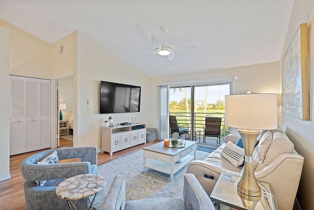 living area with a ceiling fan, lofted ceiling, light wood-style flooring, and a textured ceiling