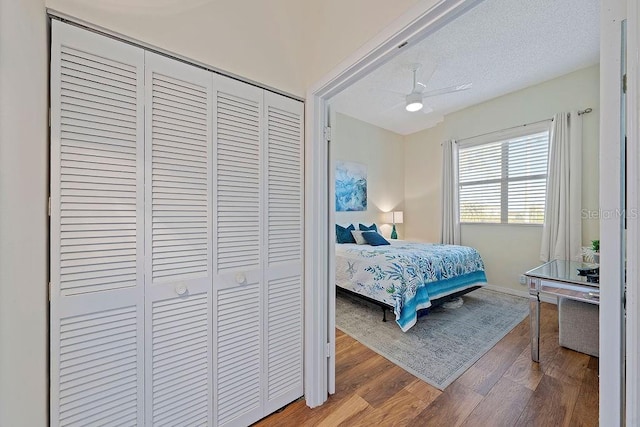 bedroom with a textured ceiling, a closet, a ceiling fan, and wood finished floors