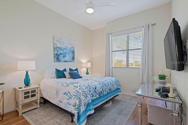 bedroom with ceiling fan, a textured ceiling, baseboards, and wood finished floors