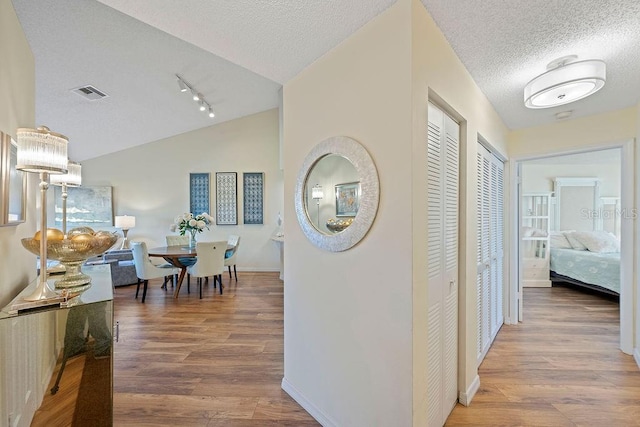 hall with visible vents, vaulted ceiling, a textured ceiling, and wood finished floors