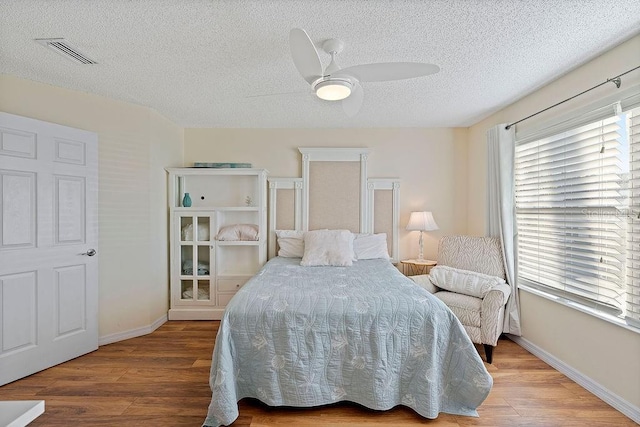 bedroom with a textured ceiling, wood finished floors, visible vents, and baseboards