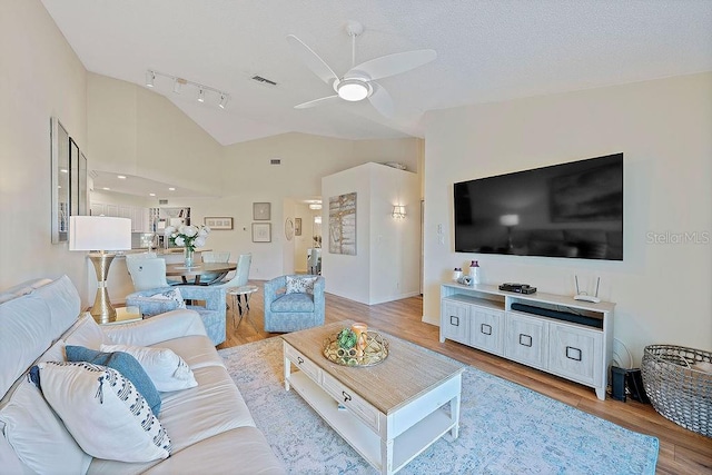 living room with lofted ceiling, track lighting, light hardwood / wood-style floors, and ceiling fan