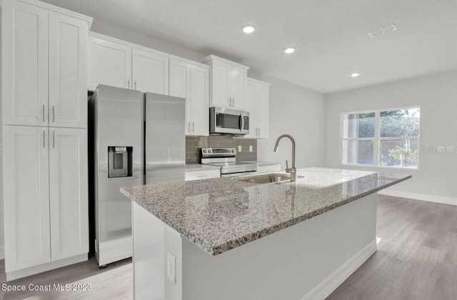 kitchen with white cabinets, appliances with stainless steel finishes, a center island with sink, and sink