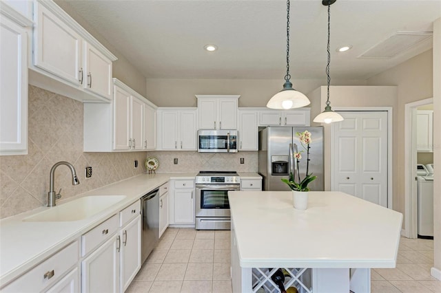 kitchen with hanging light fixtures, sink, appliances with stainless steel finishes, white cabinetry, and washing machine and clothes dryer