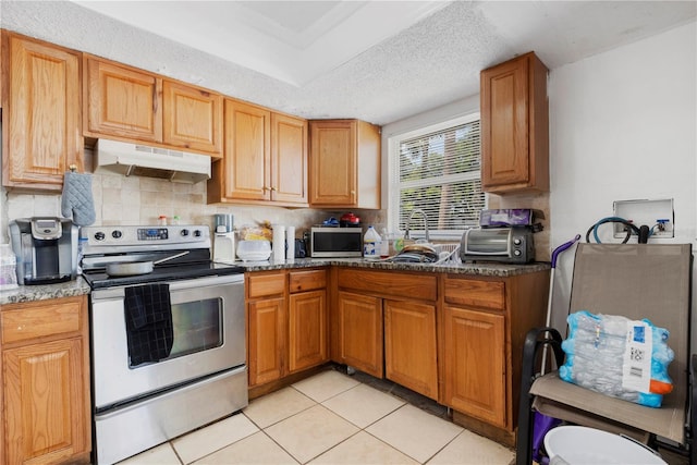 kitchen with dark stone counters, sink, light tile patterned floors, a textured ceiling, and appliances with stainless steel finishes