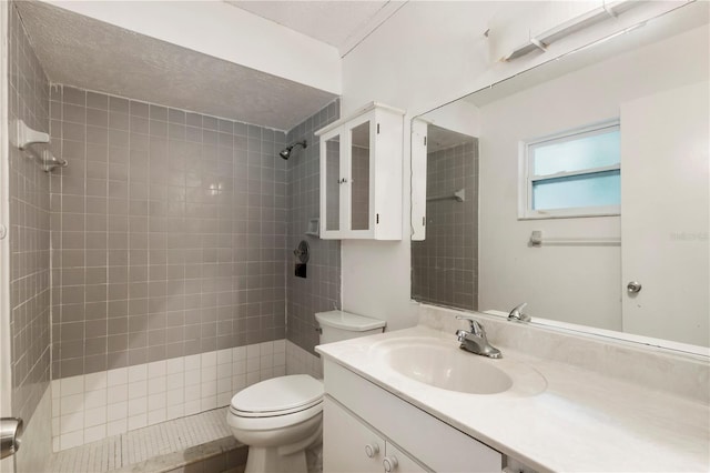 bathroom featuring a tile shower, vanity, a textured ceiling, and toilet