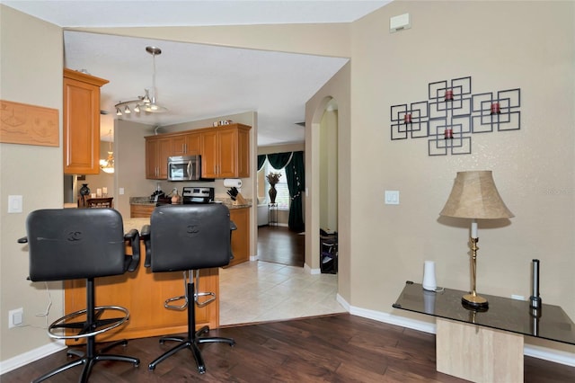 kitchen with a kitchen bar, vaulted ceiling, hanging light fixtures, light hardwood / wood-style flooring, and appliances with stainless steel finishes