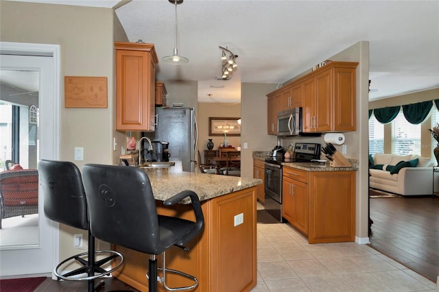 kitchen with light tile patterned flooring, appliances with stainless steel finishes, a breakfast bar, pendant lighting, and light stone countertops