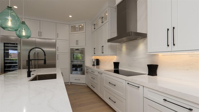 kitchen featuring light wood-type flooring, light stone counters, wall chimney exhaust hood, double oven, and white cabinetry