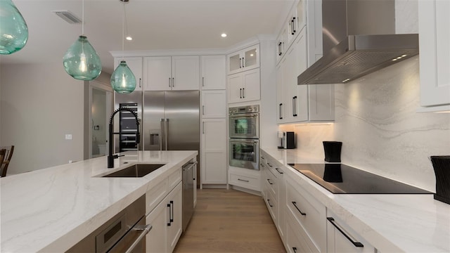 kitchen with white cabinets, sink, hanging light fixtures, wall chimney exhaust hood, and stainless steel appliances