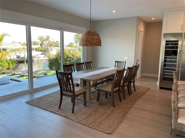 dining room with wine cooler, a water view, and light wood-type flooring