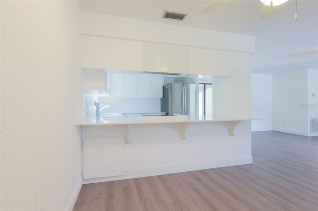 kitchen featuring white cabinets, kitchen peninsula, a breakfast bar area, and stainless steel refrigerator