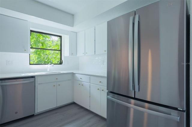 kitchen with white cabinets, sink, decorative backsplash, appliances with stainless steel finishes, and light hardwood / wood-style floors