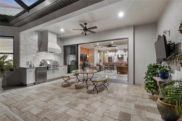 patio terrace at dusk featuring grilling area, ceiling fan, and exterior kitchen