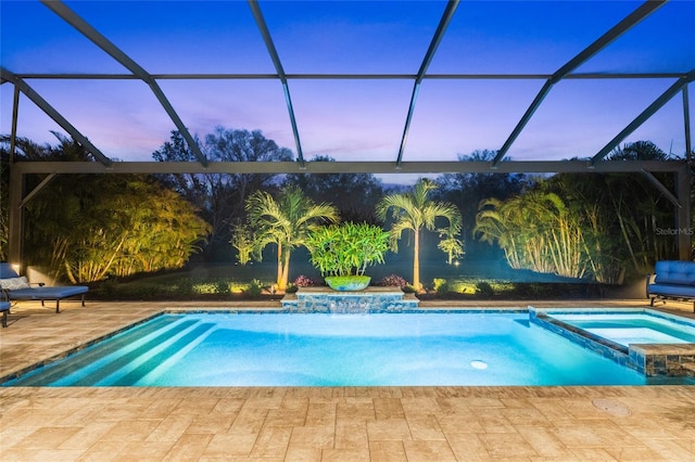 pool at dusk with an in ground hot tub, a lanai, and a patio