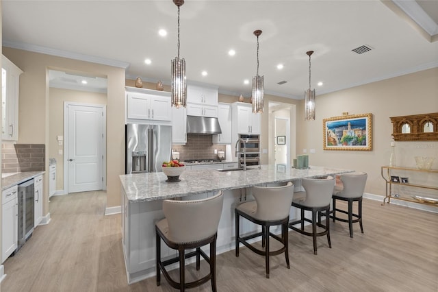 kitchen featuring hanging light fixtures, a large island with sink, white cabinets, and appliances with stainless steel finishes