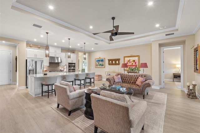 living room with ornamental molding, ceiling fan, light wood-type flooring, and a tray ceiling