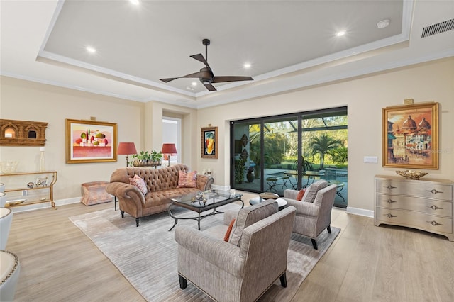 living room featuring a raised ceiling, crown molding, and light wood-type flooring