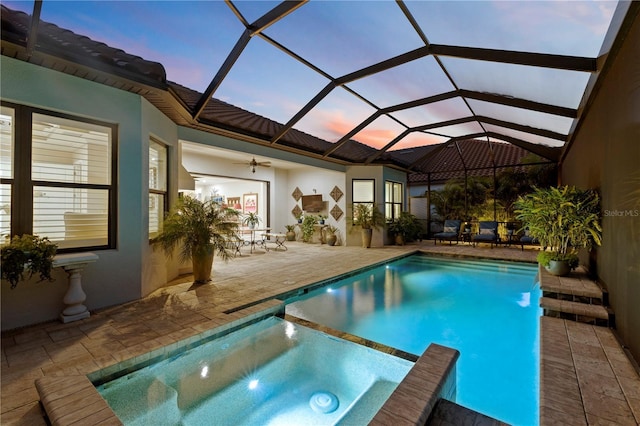 pool at dusk with an in ground hot tub, a lanai, ceiling fan, and a patio area