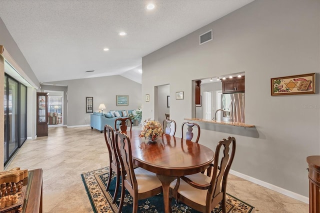 dining space featuring a textured ceiling, sink, light tile patterned flooring, and vaulted ceiling